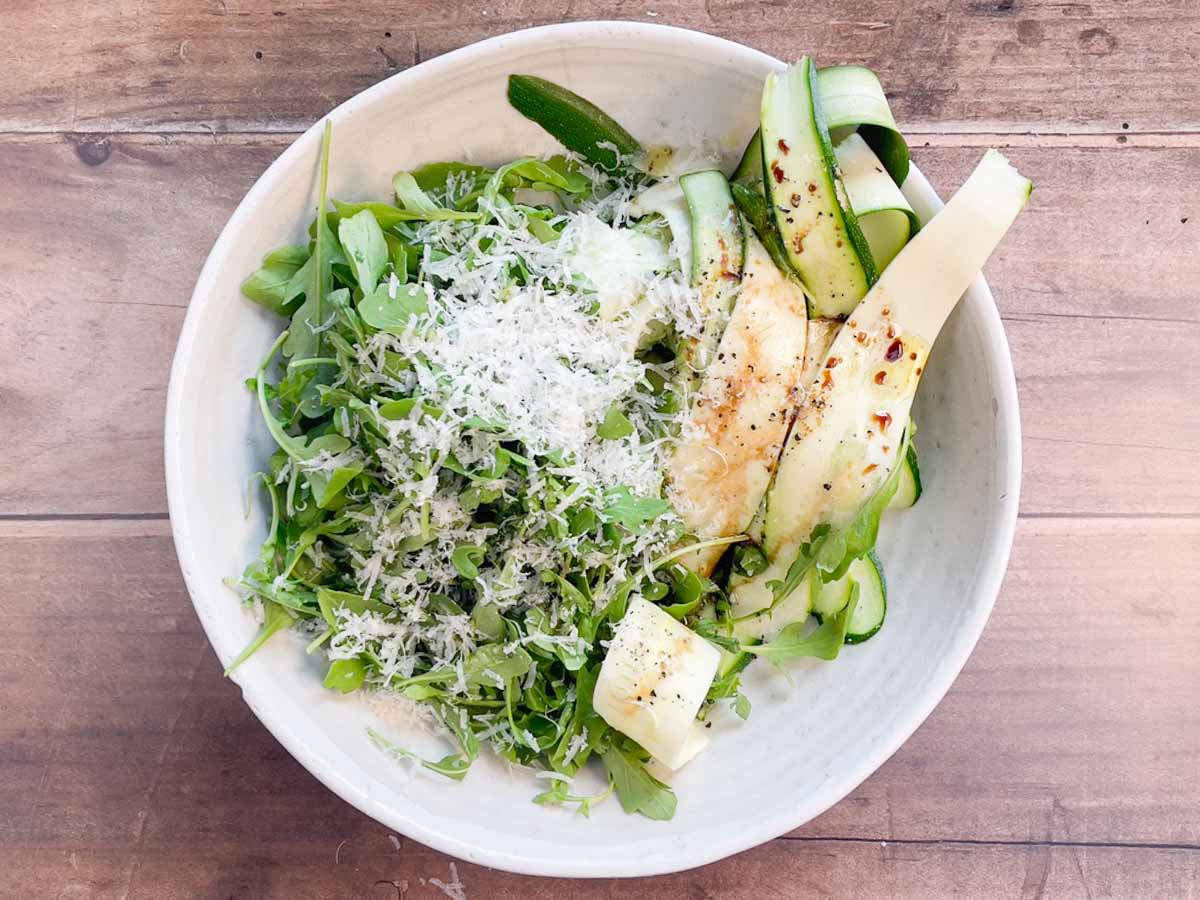 long zucchini strips, arugula, parmesan and dressing in a bowl